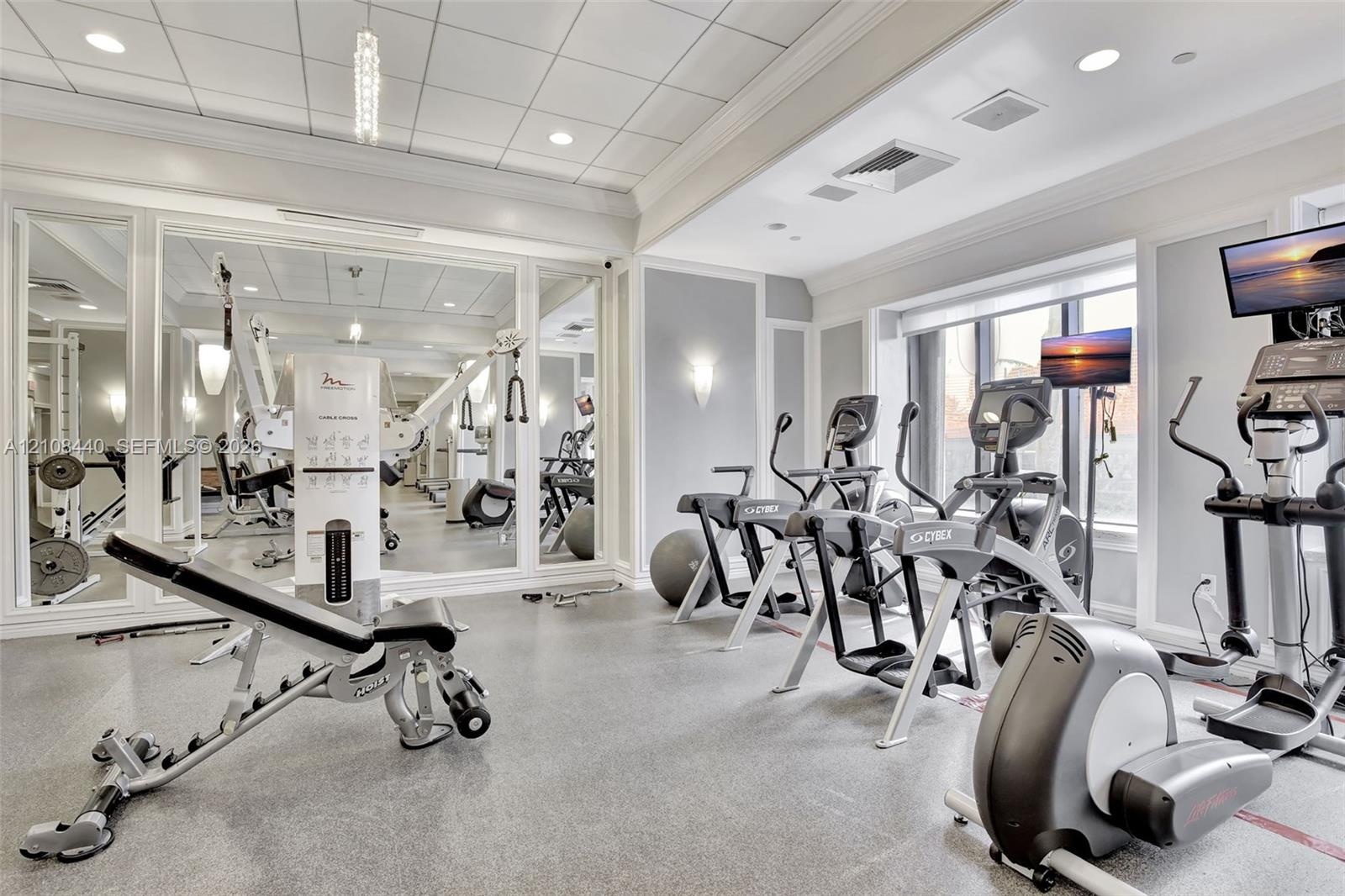 Fitness space featuring floor-to-ceiling mirrors, a coffered ceiling with recessed lighting, wall-mounted sconces, and impact-resistant rubber floorin