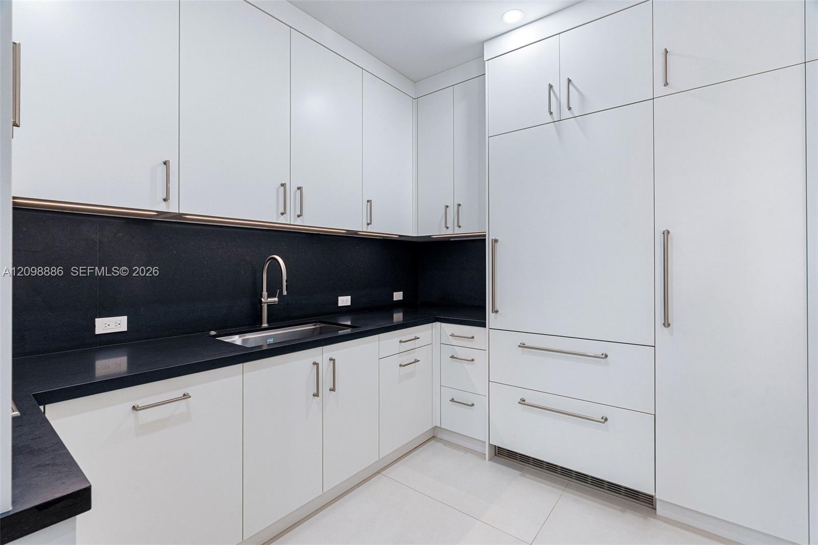 Kitchen featuring flat-panel white cabinetry, contrasting dark stone countertops, integrated panel-ready refrigerator, stainless steel undermount sink