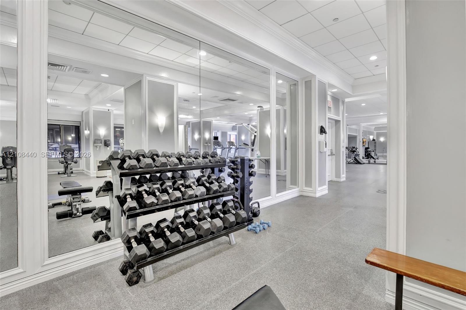 Fitness facility featuring wall-to-wall mirrors, recessed lighting, drop ceiling panels, and durable composite flooring