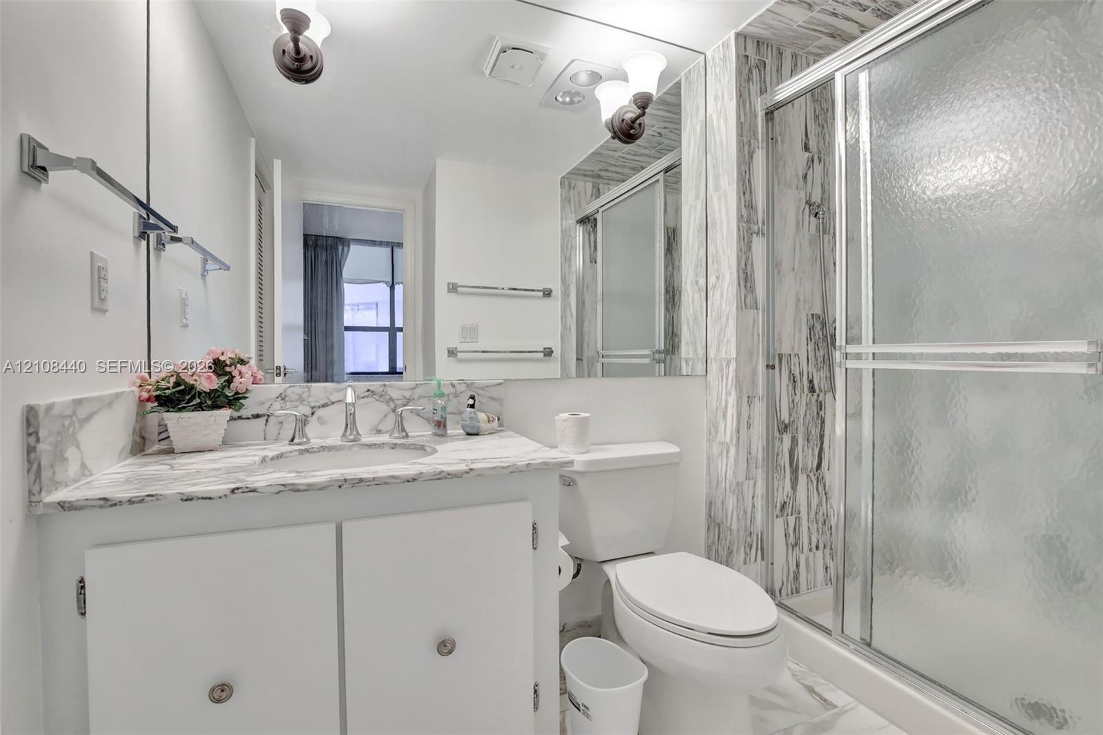 Bathroom featuring a stone-surface vanity with an integrated sink, floor-to-ceiling stone-tiled shower enclosure, chrome-finish sliding glass shower d