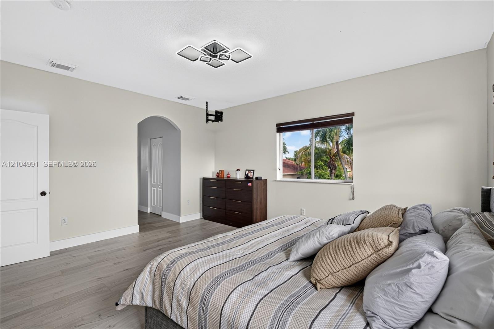 Wood-finish flooring, geometric ceiling lighting, arched entryway, and single-hung window with dark window treatments