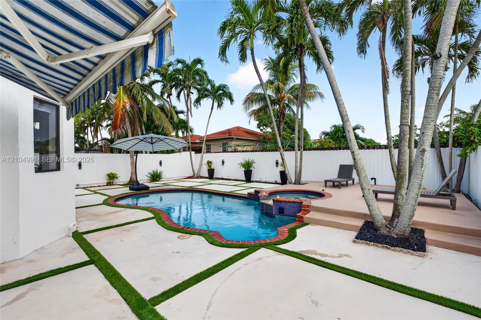 In-ground pool with integrated spa, paver patio with turf detailing, retractable fabric awning, and perimeter privacy fencing