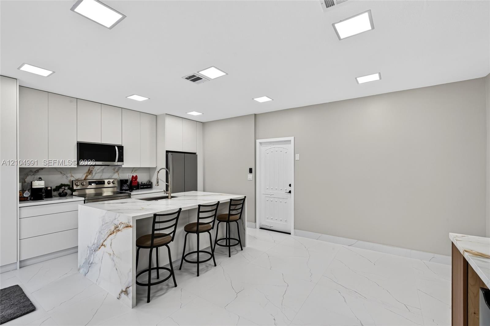 Kitchen featuring floor-to-ceiling cabinetry, a waterfall-edge island with stone-finish countertops, large-format tile flooring, and integrated square