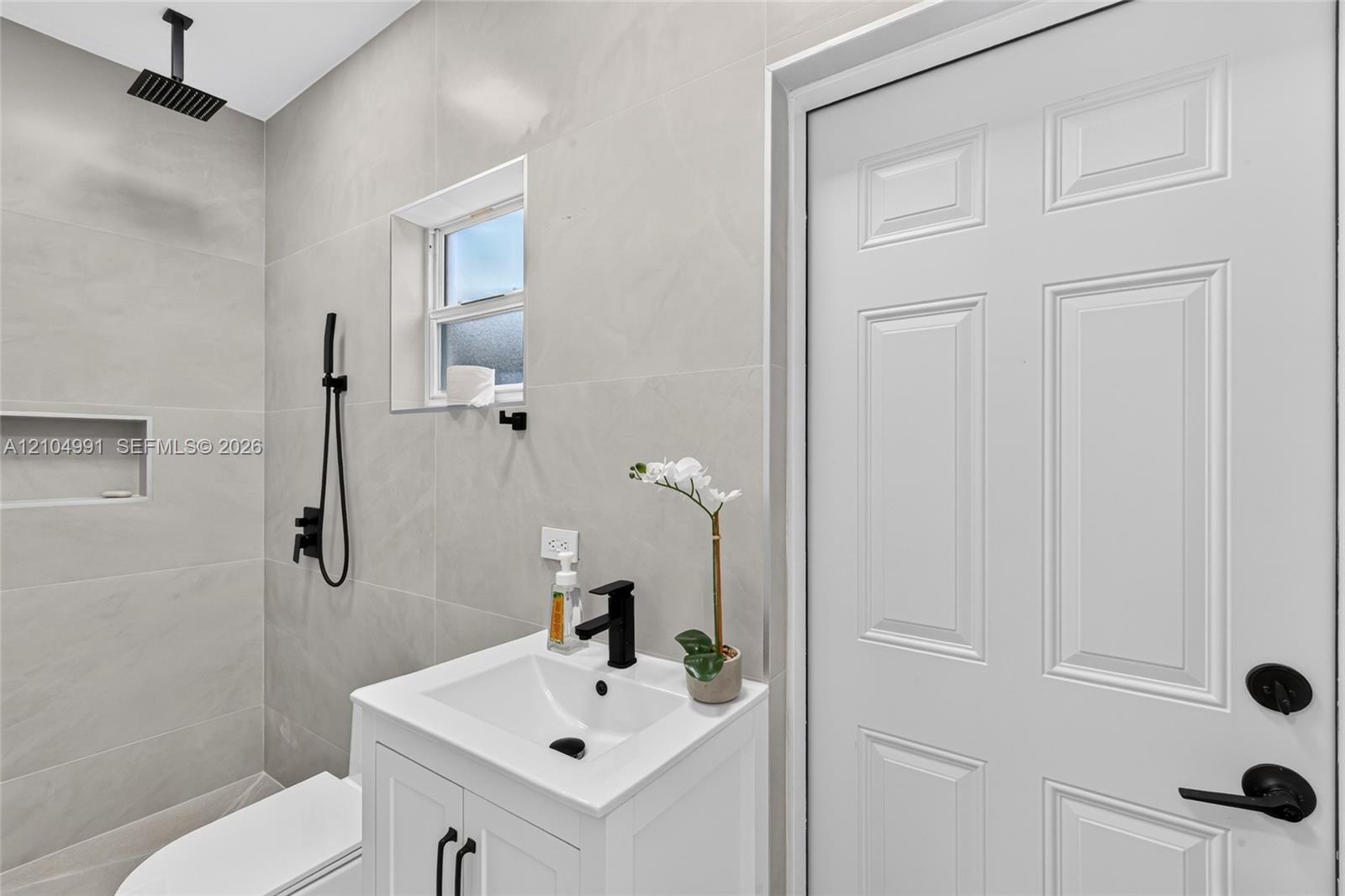 Full-height neutral wall tiling, walk-in shower with rainfall showerhead and built-in wall niche, white vanity with rectangular basin and matte black 