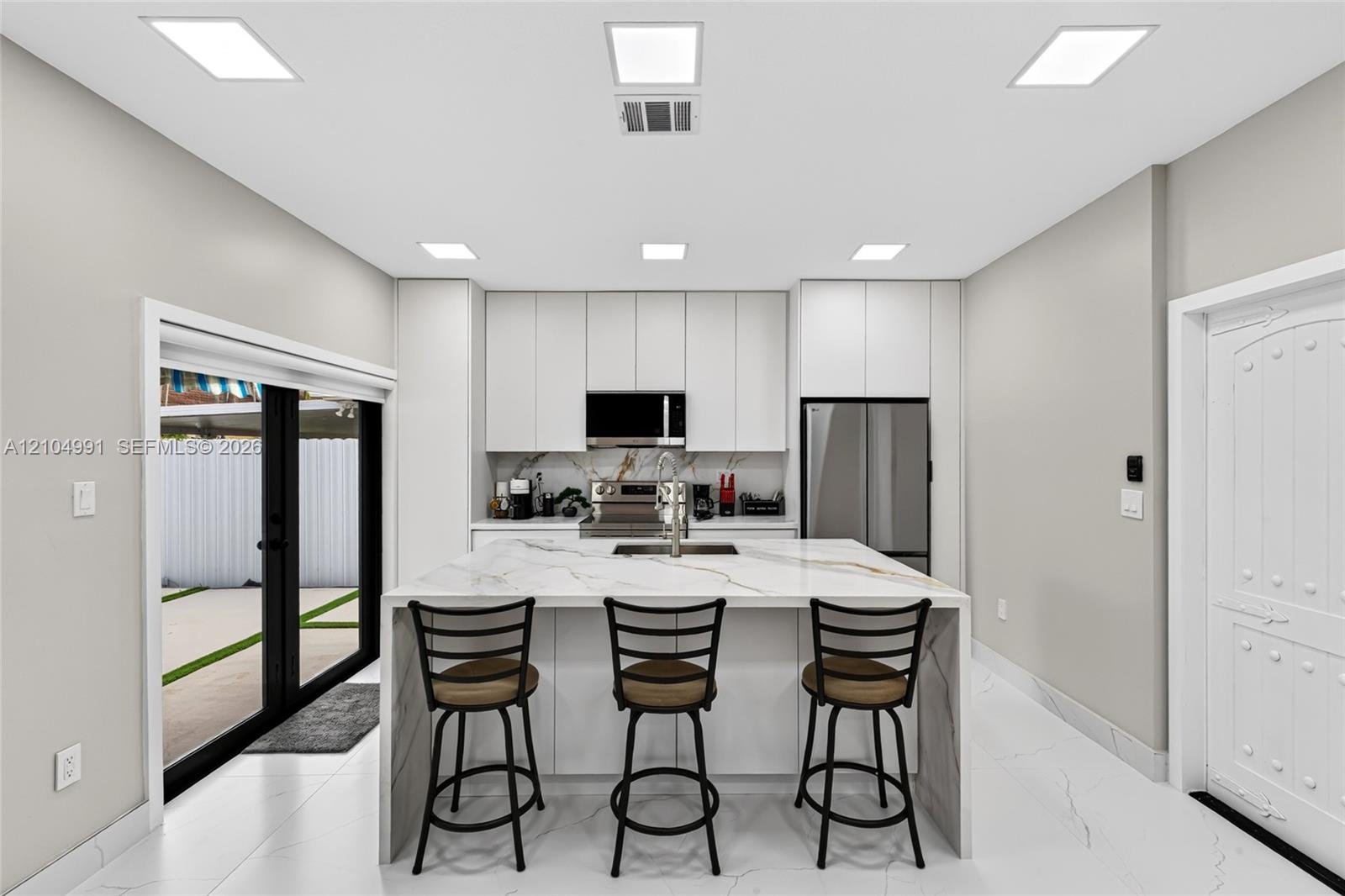 Kitchen featuring floor-to-ceiling cabinetry, a central island with a waterfall-edge countertop, stainless steel appliances, recessed lighting, and la