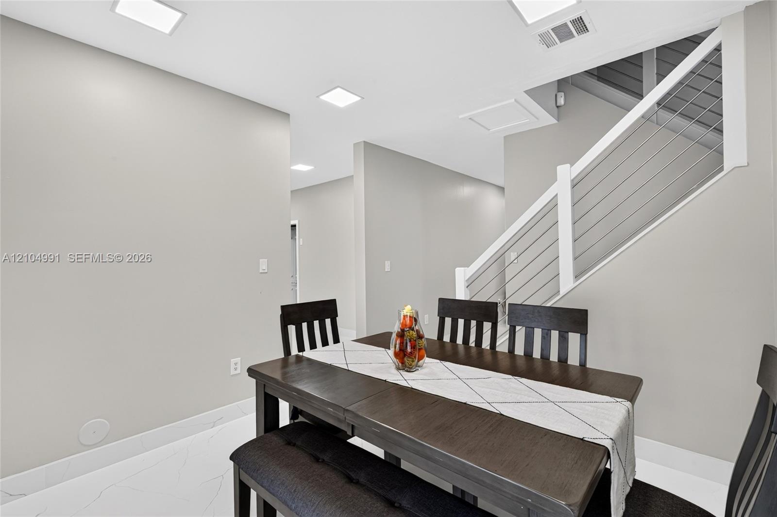 Interior space featuring large-format tile flooring, recessed ceiling lighting, and a staircase with a white handrail and horizontal metal cable raili