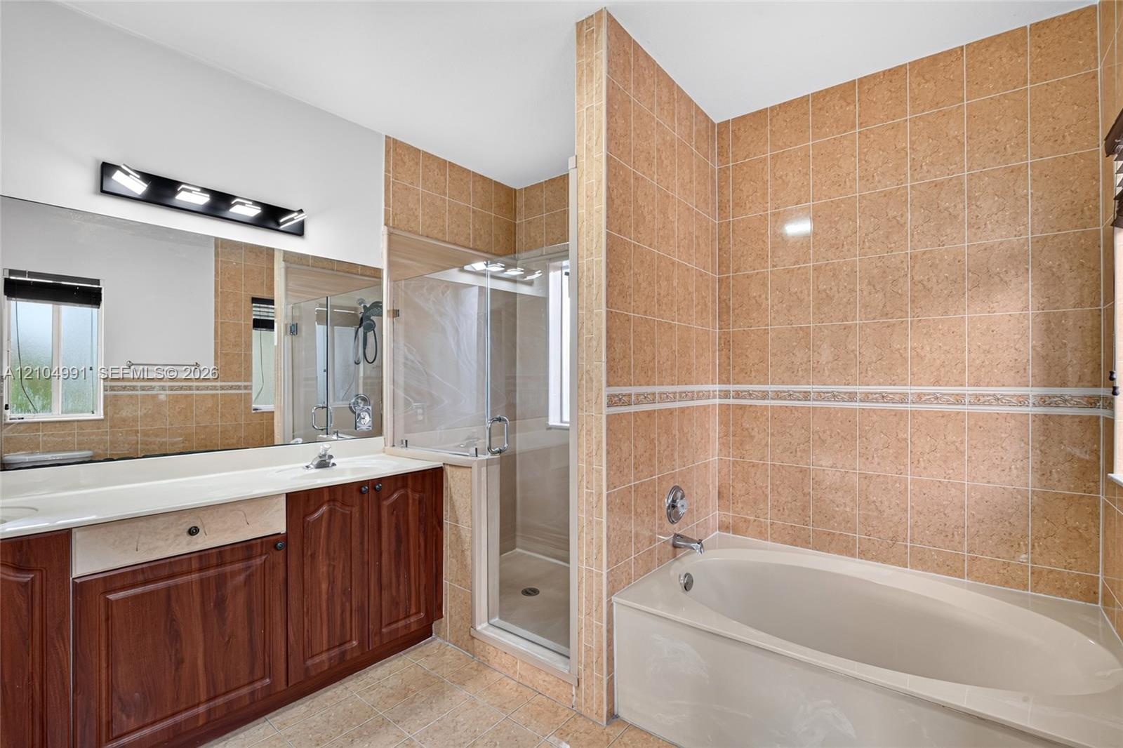 Bathroom featuring a wood-finish vanity with a light-toned countertop, a soaking tub with tile surround, a glass-enclosed shower, a large wall-mounted