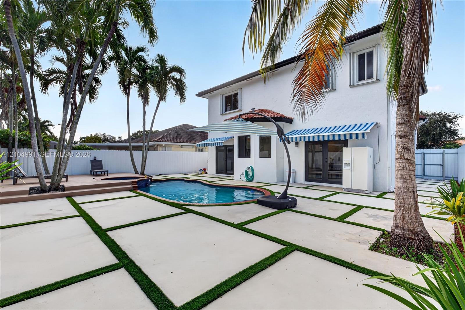 Backyard featuring an in-ground swimming pool, raised composite deck, custom concrete paver patio with turf detailing, and privacy fencing