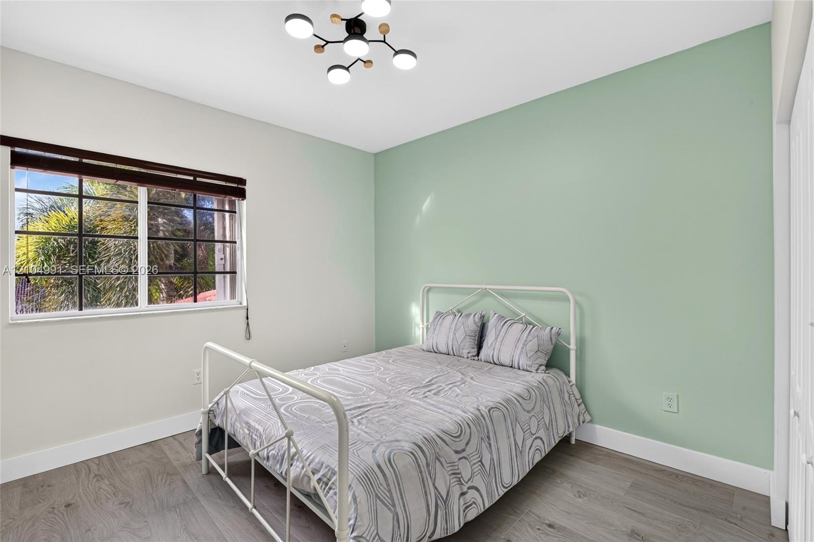 Room featuring wood-finish flooring, a contemporary multi-light fixture, an accent wall, and a multi-pane window with a horizontal blind
