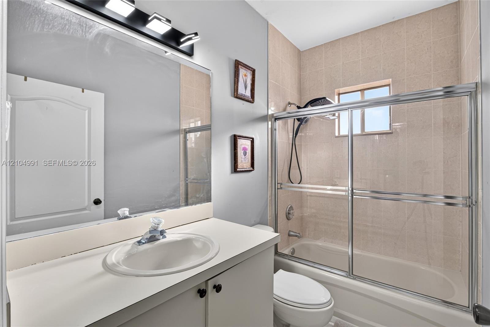 Bathroom featuring a vanity with a white countertop and oval basin, wall-mounted vanity lighting, a full-width mirror, and a tub-shower combination wi