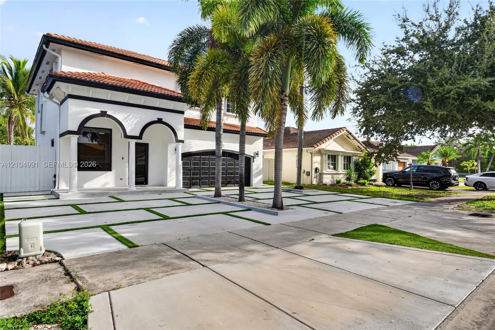 Two-story stucco exterior featuring arched entryways, a tiled roof, multi-car garage, and a concrete paver driveway with integrated green space