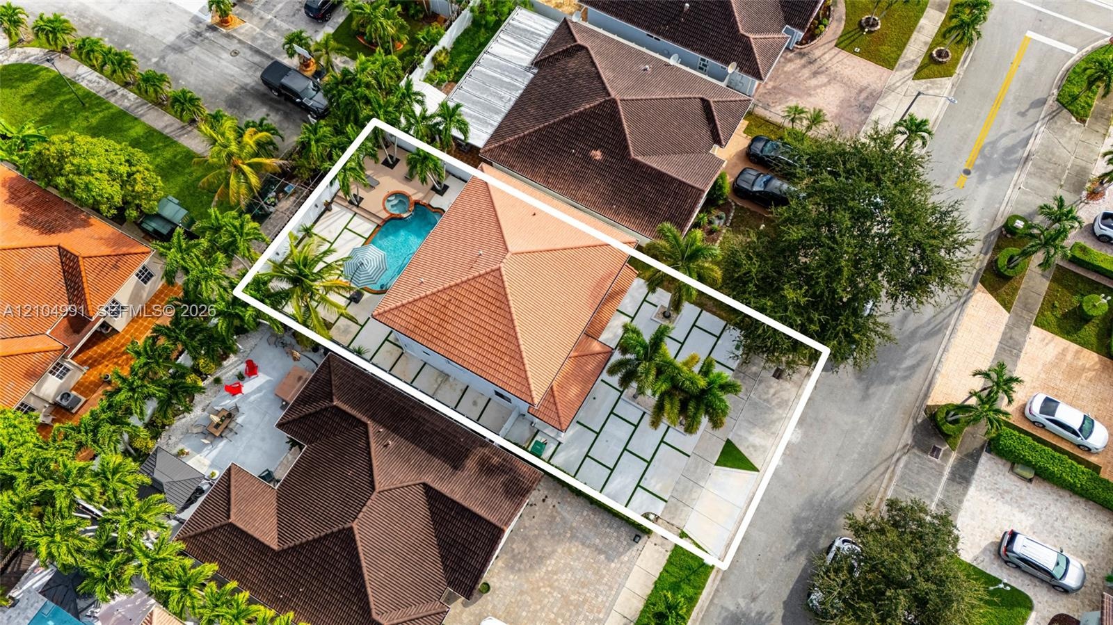Aerial view featuring a tile roof, an in-ground swimming pool with an attached spa, and geometric concrete pavers