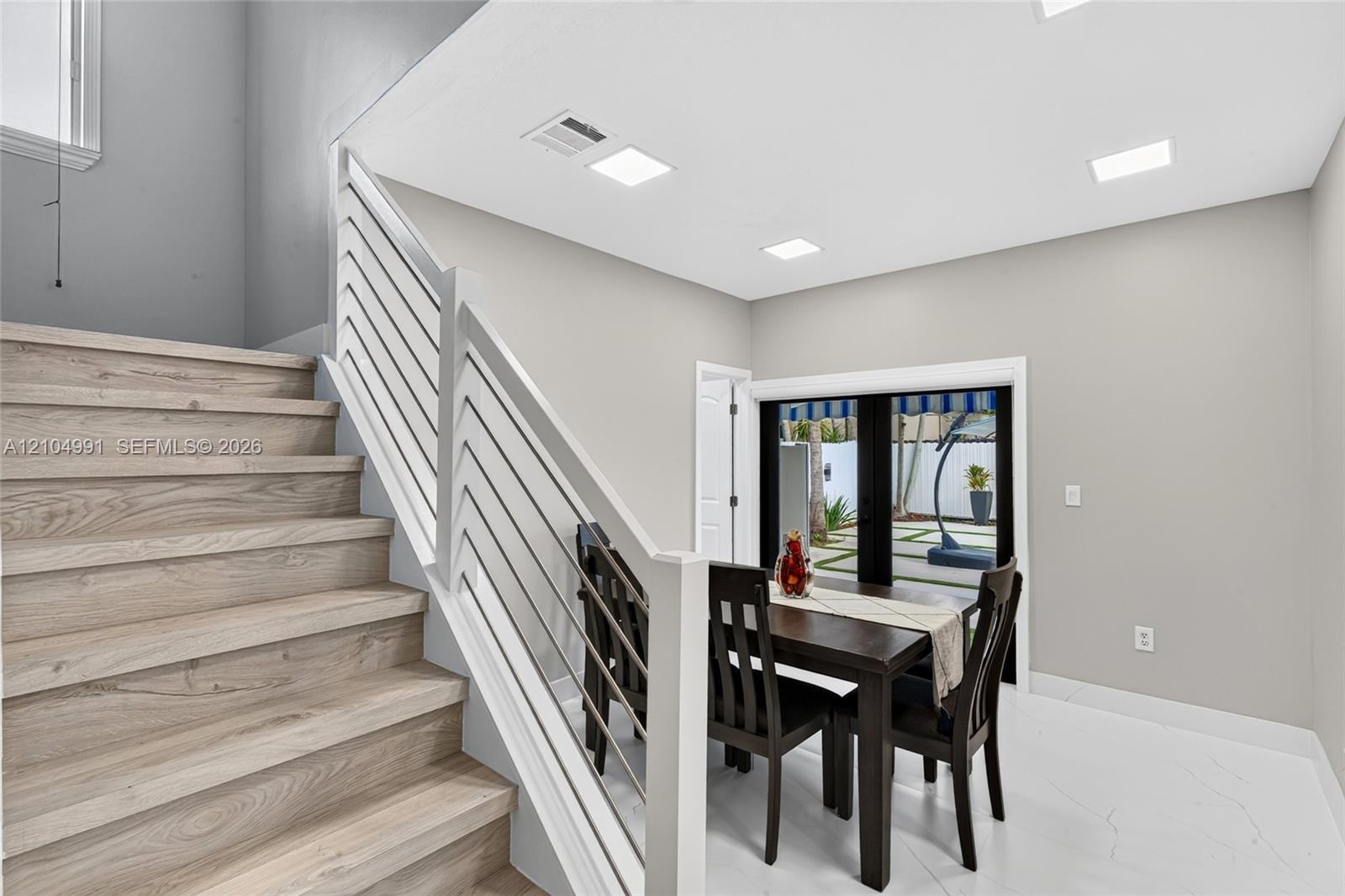 Staircase featuring wood-finish treads, custom white horizontal metal railing, recessed ceiling lighting, and large-format tile flooring