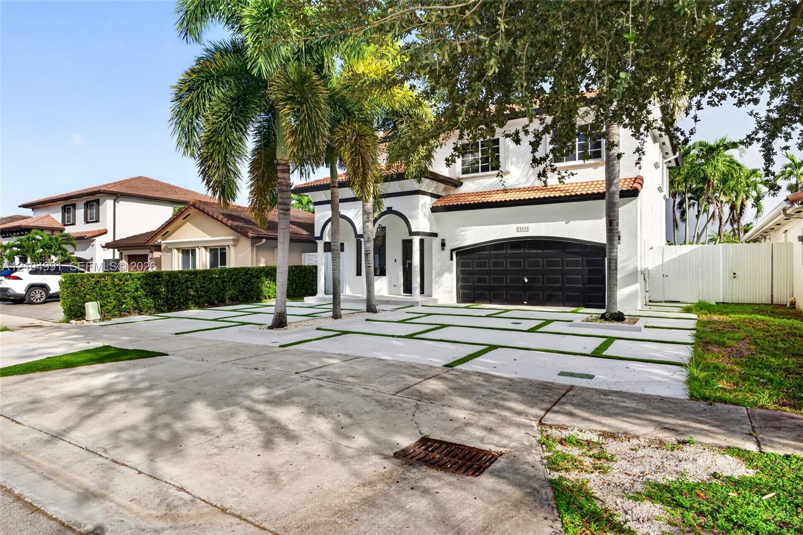Two-story exterior featuring white stucco finish, arched entryways, multi-car garage with dark metal doors, tile roof, and a paved driveway with integ