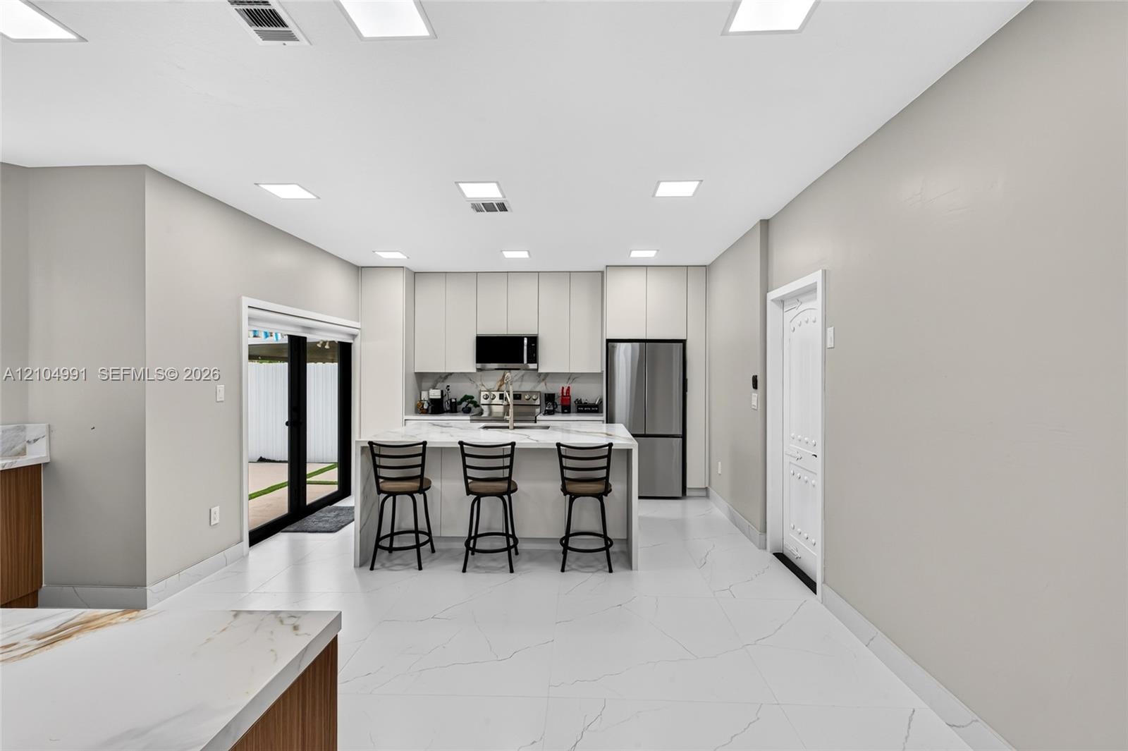Kitchen featuring floor-to-ceiling cabinetry, a central island with a stone-surface countertop, stainless steel appliances, and large-format tile floo