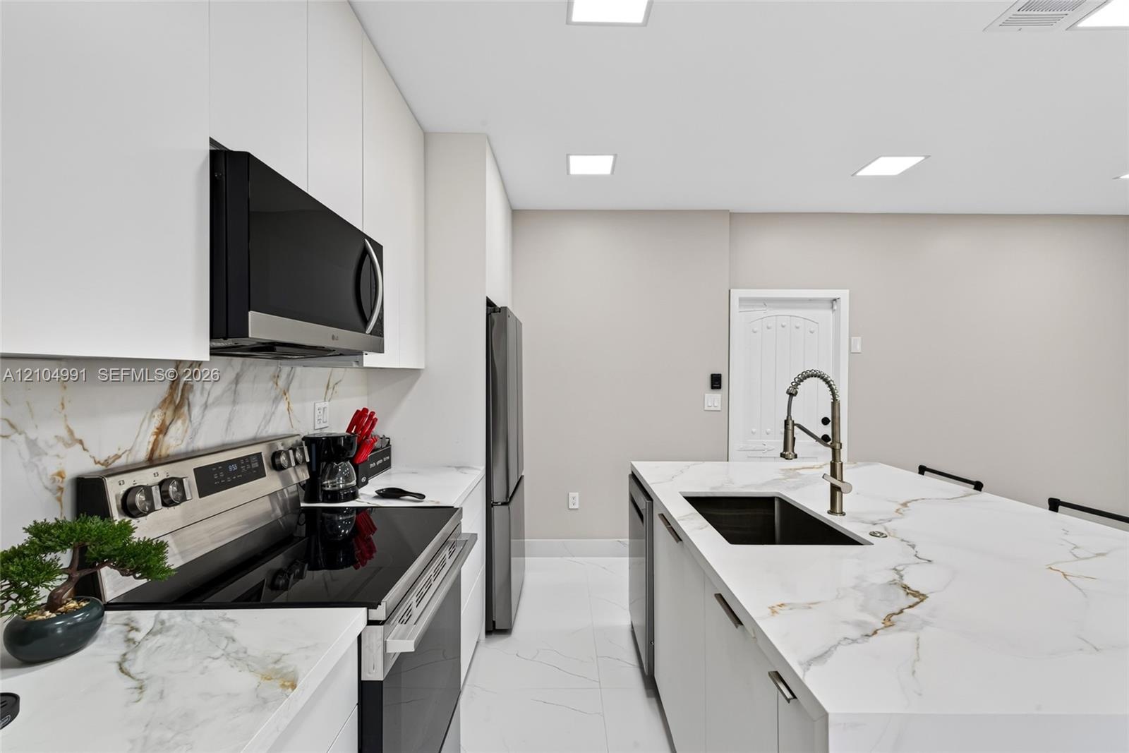 Kitchen featuring white slab cabinetry, large-format tiled flooring, stone-finish countertops with matching full-height backsplash, stainless steel ap