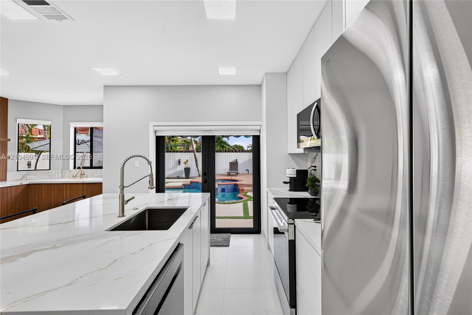 Kitchen featuring a central island with a stone-finish countertop and undermount sink, stainless steel appliances, flat-panel cabinetry, and black-fra