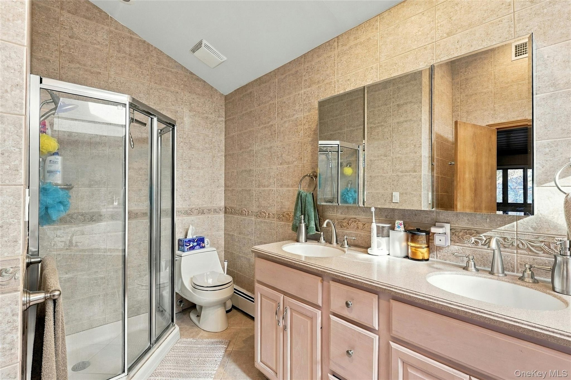 Bathroom featuring a double-sink vanity with a solid-surface countertop, tiled wall surfaces, and a glass-enclosed shower