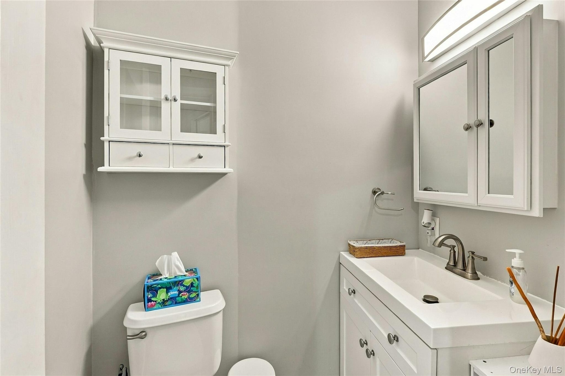 White vanity with integrated rectangular sink and metallic faucet, complemented by a mirrored medicine cabinet, wall-mounted light fixture, and white 