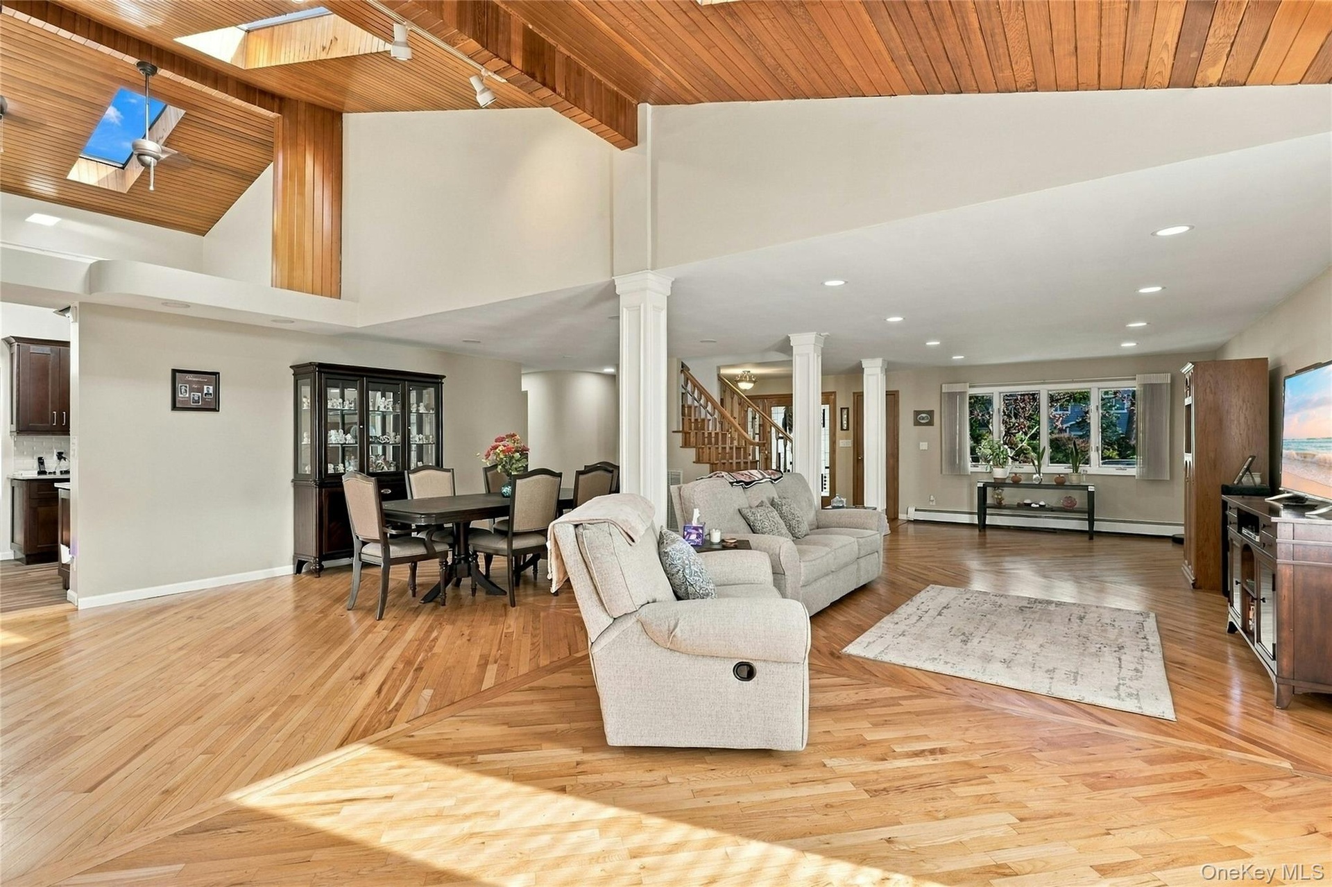 Vaulted wood-plank ceiling, skylights, recessed lighting, structural support columns, and wood-finish flooring