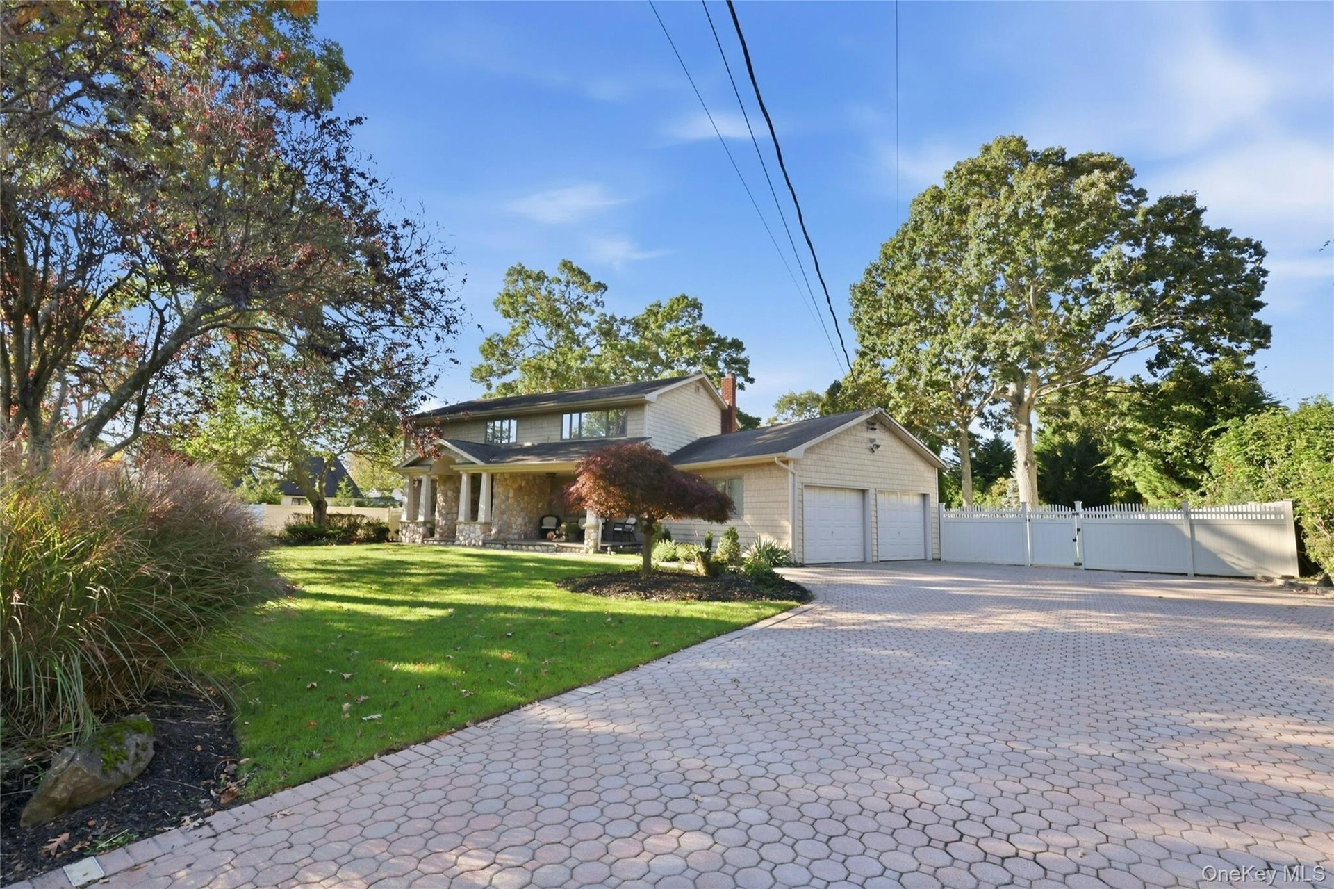 Two-story exterior featuring stone masonry cladding and an expansive paved driveway, set upon a landscaped lot with mature trees and perimeter fencing