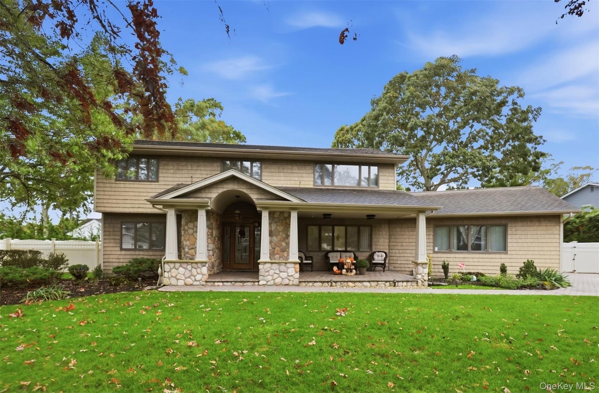Two-story shingle-style exterior featuring a covered front porch with stone pillars, a stone-accented entryway, and a paved walkway