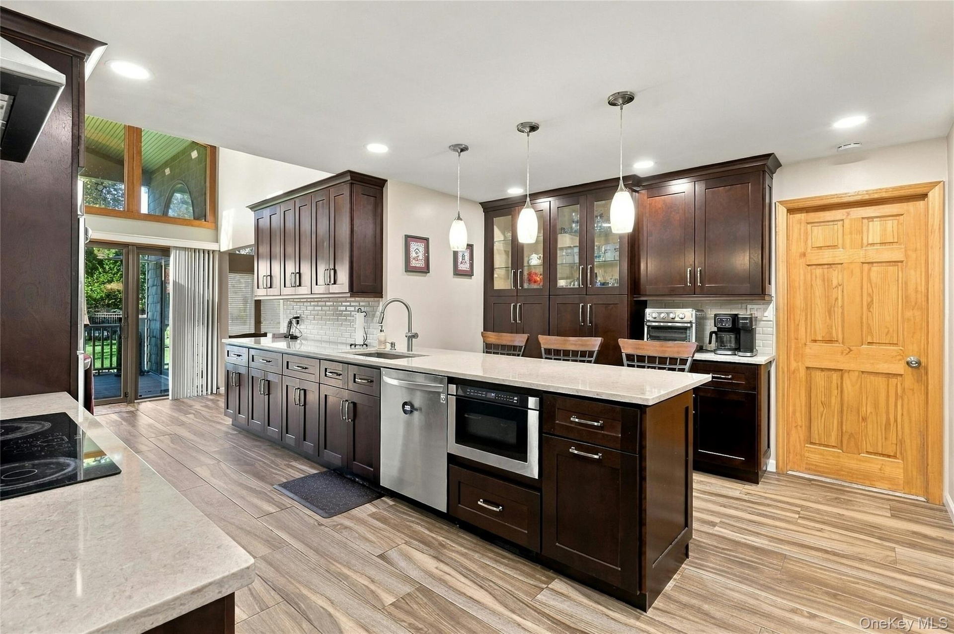 Kitchen featuring dark wood cabinetry, light-toned stone countertops, a central island with integrated microwave, wood-finish flooring, and pendant li