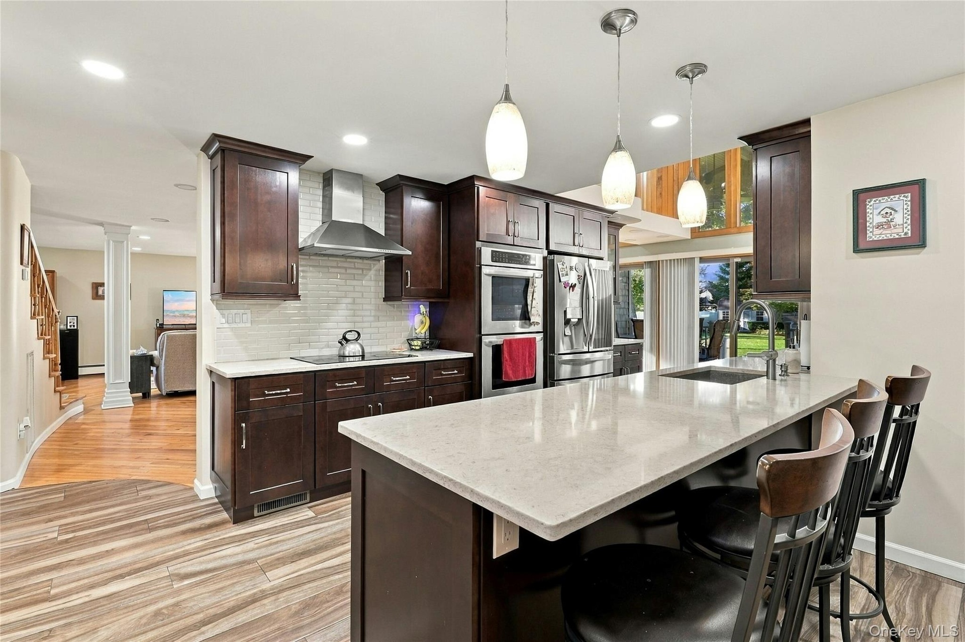Kitchen featuring dark wood cabinetry, quartz countertops, a central island with a stainless steel undermount sink, subway tile backsplash, and built-