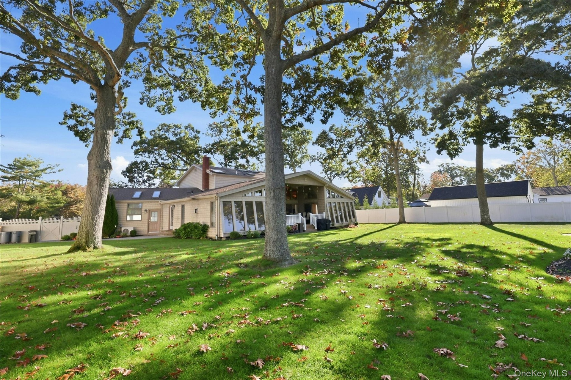 Expansive backyard featuring mature hardwood trees, a manicured lawn, full-height privacy fencing, and a multi-pane glass sunroom addition