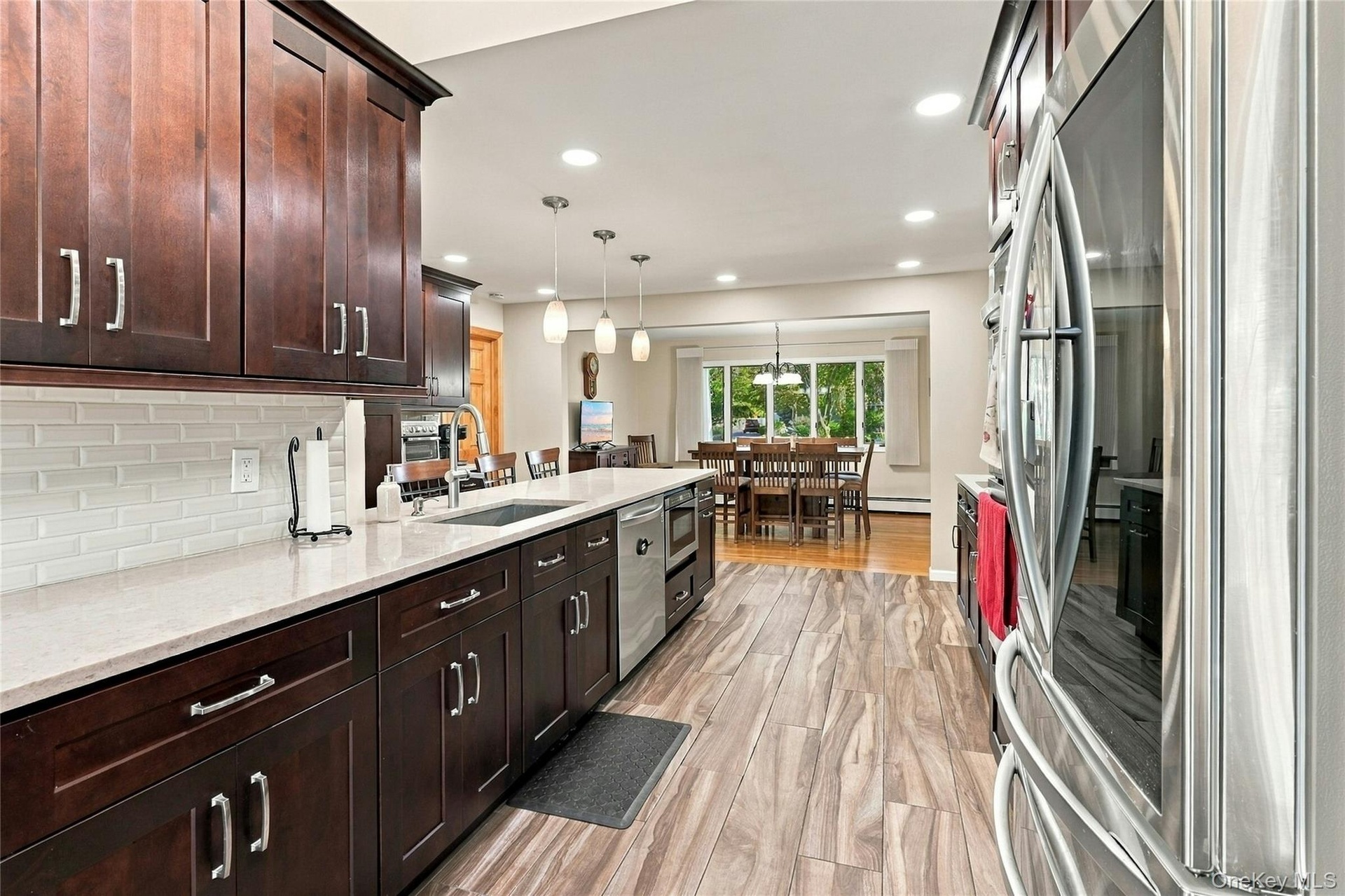 Kitchen featuring stained wood cabinetry, stone countertops, white subway tile backsplash, wood-finish flooring, and stainless steel appliances