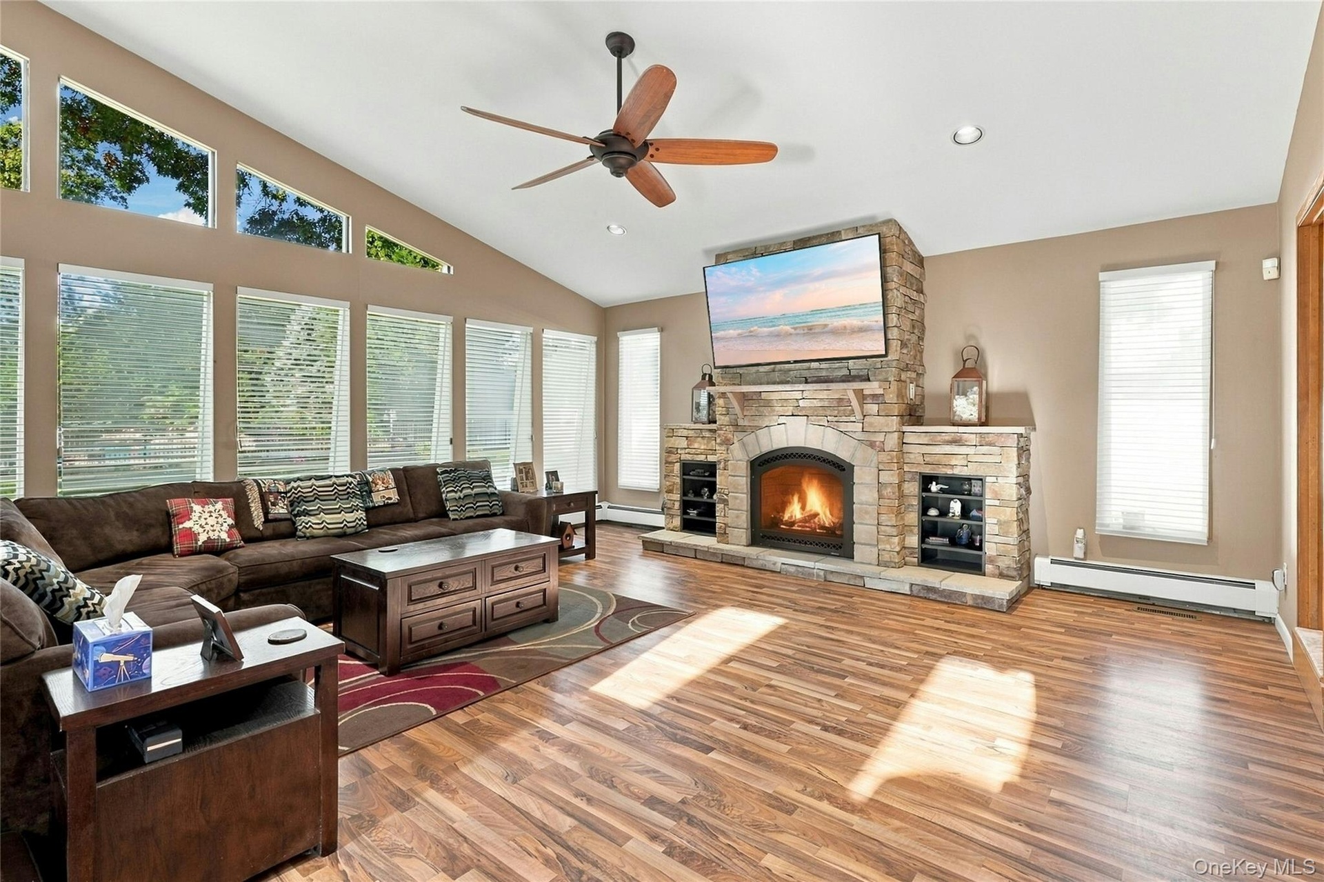 Living room featuring vaulted ceilings, floor-to-ceiling stone-faced fireplace with hearth, wood-finish flooring, multi-pane window configuration, and