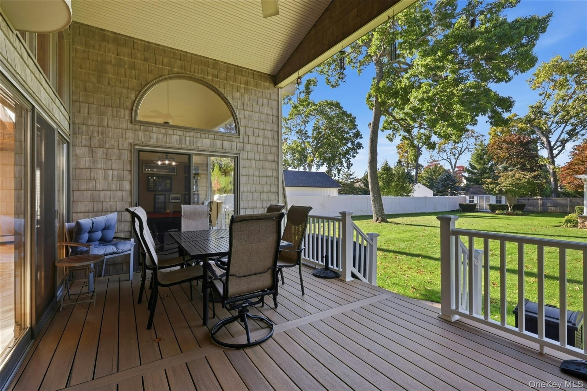 Covered deck featuring composite decking, arched transom window, shingle-style exterior siding, white railing, and expansive lawn