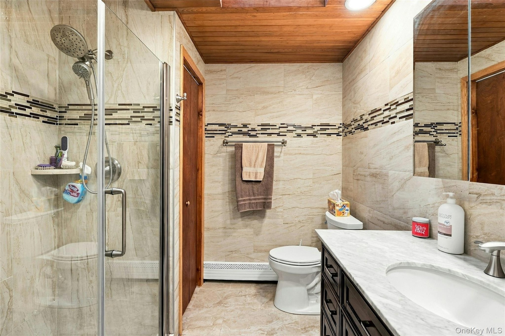 Bathroom featuring a walk-in shower with glass enclosure, wood-paneled ceiling, stone-finish wall tile with mosaic accent inlay, and vanity with stone