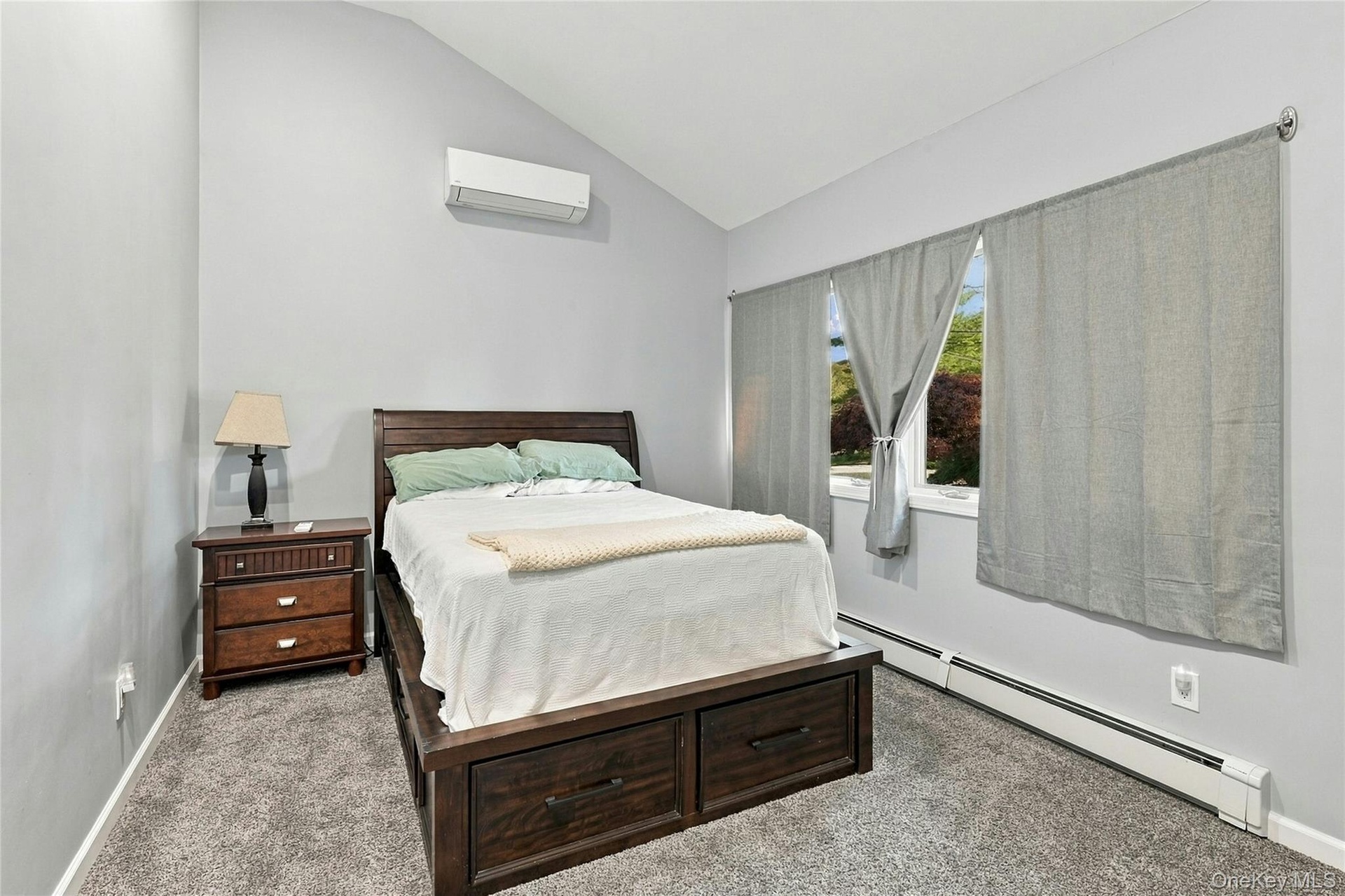 Vaulted ceilings featuring a wall-mounted ductless heating and cooling unit, neutral carpeting, and a window with hardware