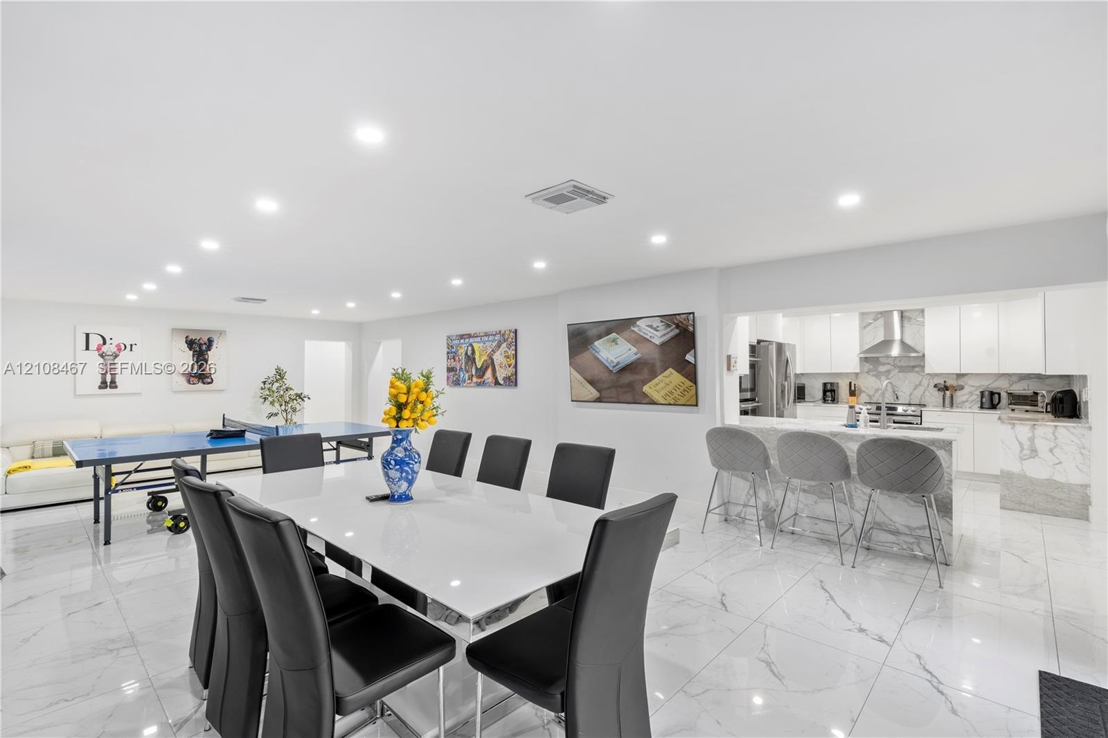 Large-format tile flooring, recessed ceiling lighting, and a kitchen featuring a stone-finish waterfall edge peninsula, white cabinetry, and stainless