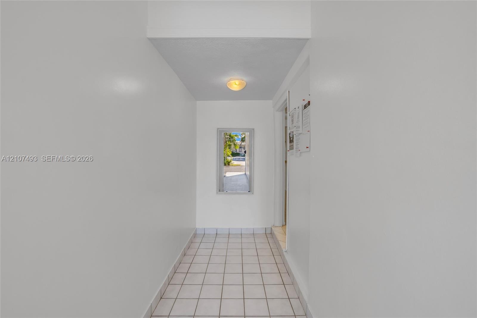 Interior hall featuring white tile flooring, neutral wall finishes, and a flush-mount light fixture
