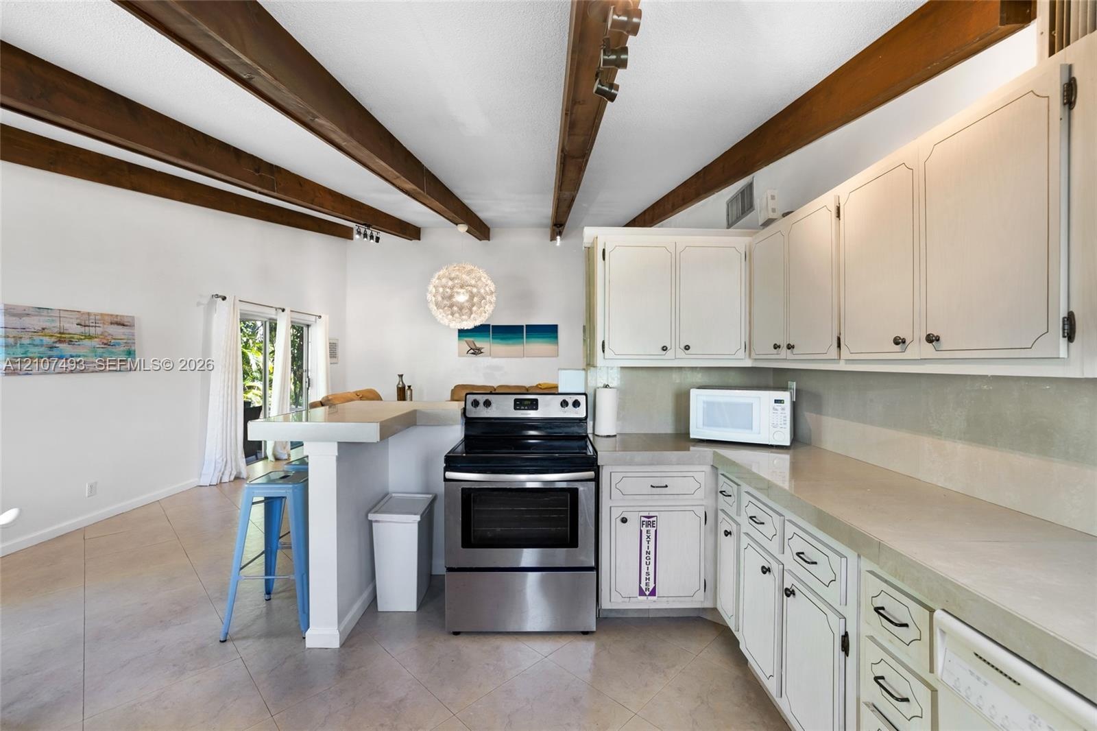 Kitchen featuring exposed wood ceiling beams, solid-surface countertops, white cabinetry, and stainless steel range