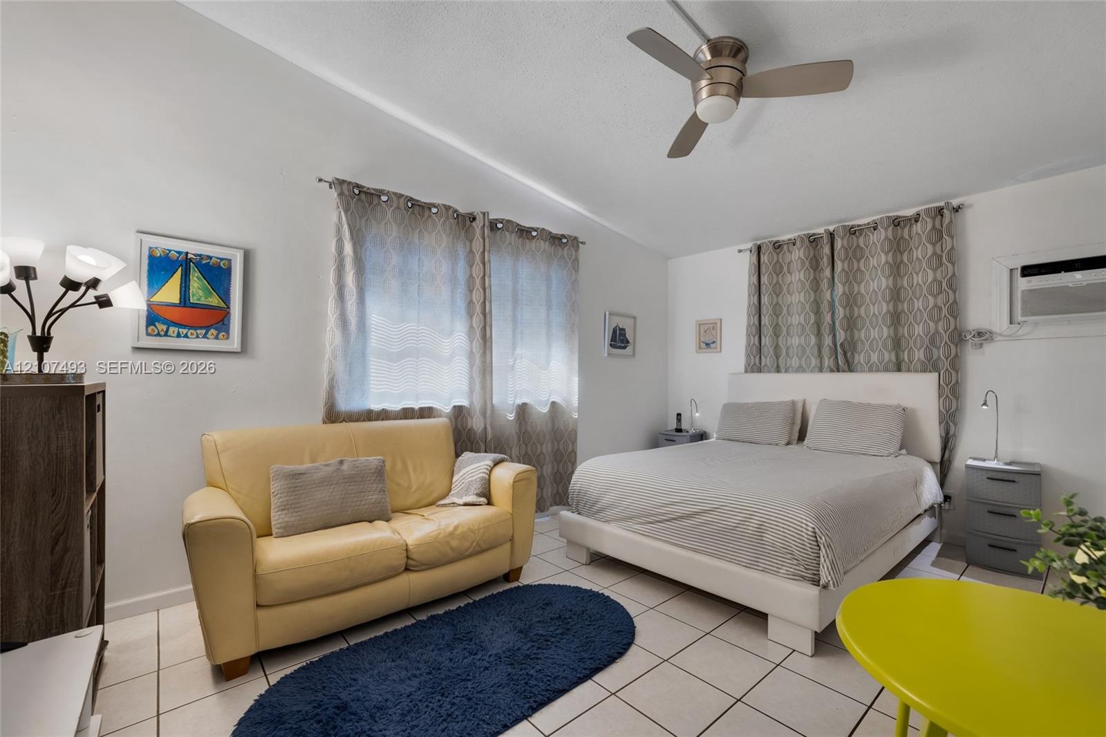 Neutral-toned interior space featuring light-colored ceramic tile flooring, a brushed metal ceiling fan, and a wall-mounted air conditioning unit