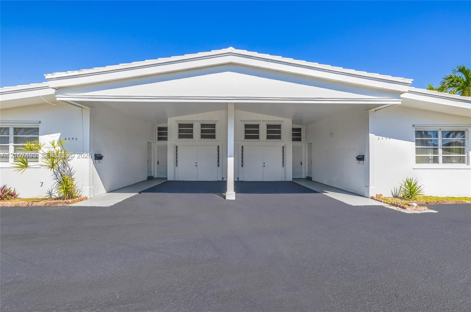 Single-story exterior featuring white stucco siding, a covered central carport, multi-pane windows, and glass block accents