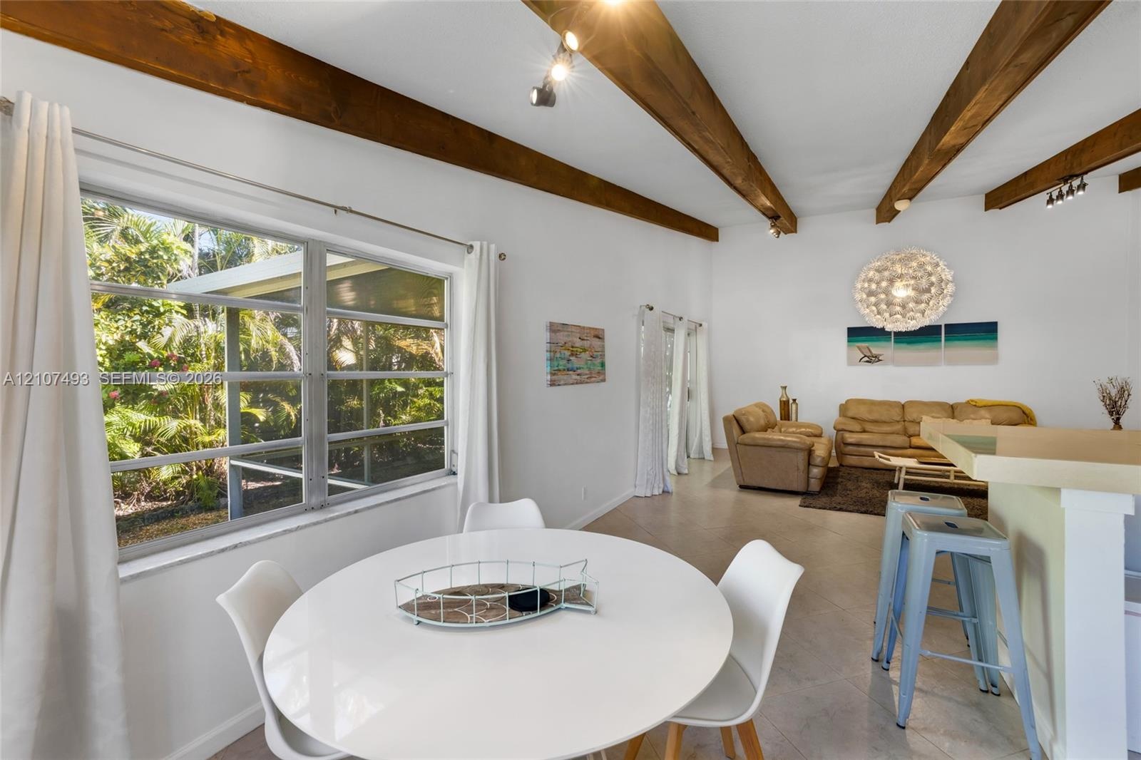 Vaulted ceiling with exposed wood beams, neutral floor tile, and large picture windows