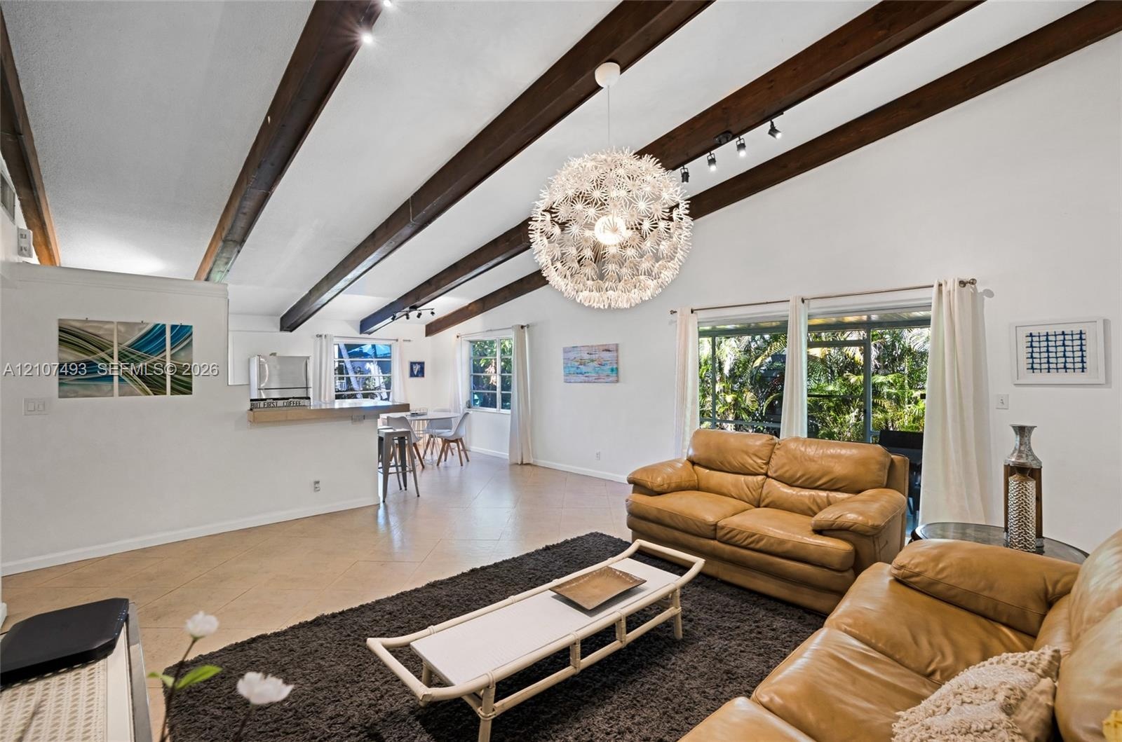 Vaulted ceiling with exposed wood beams, tile flooring, large-scale pendant lighting, and oversized windows