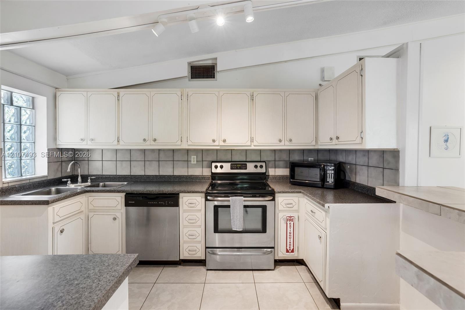 Kitchen featuring cabinetry with white shaker-style doors, stone-finish countertops, stainless steel appliances, ceramic tile backsplash, and ceramic 