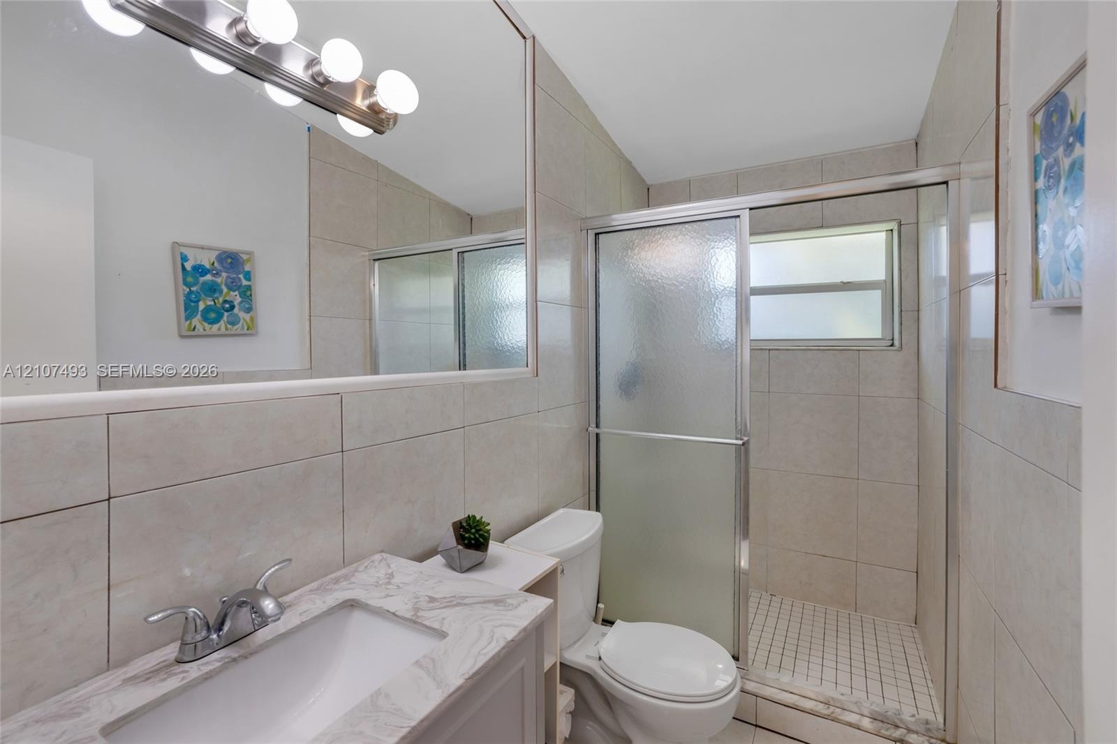 Bathroom featuring a stone-finish countertop, undermount sink, full-width vanity mirror, six-light fixture, and a tiled shower enclosure with sliding 