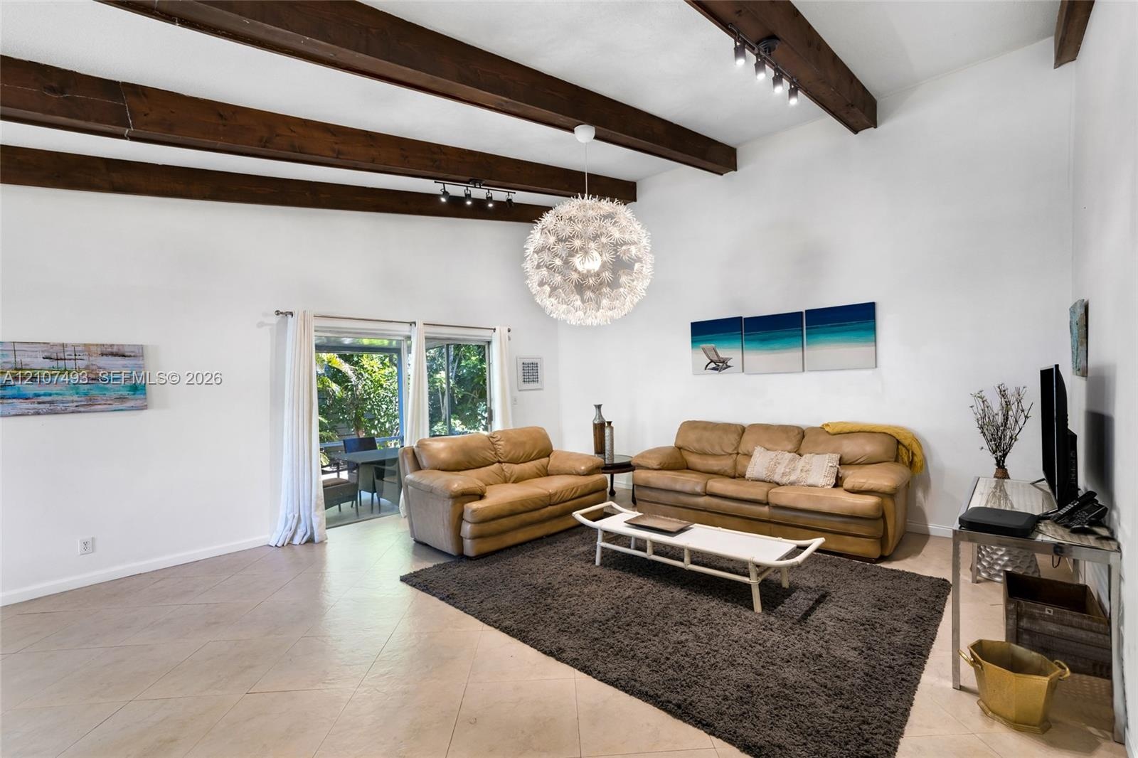 Vaulted ceilings featuring exposed dark-wood beams, neutral tile flooring, and sliding glass doors