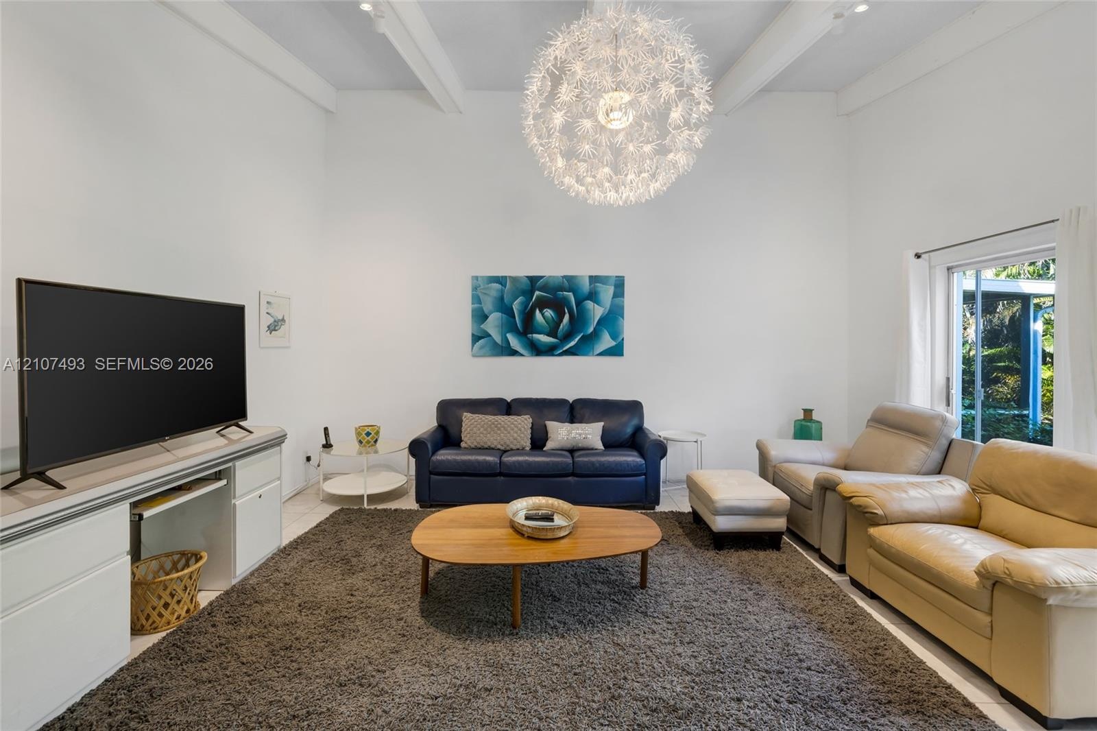 High vaulted ceilings featuring exposed structural beams, a statement spherical pendant light fixture, and floor-to-ceiling glass sliding doors