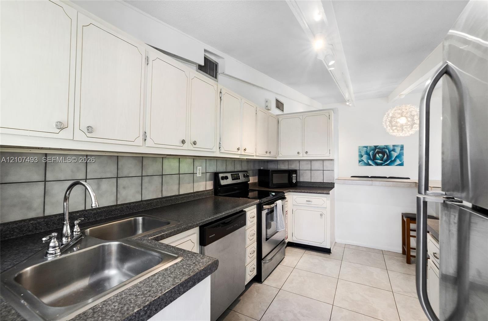 Kitchen featuring white cabinetry, dark stone-composite countertops, stainless steel appliances, a double-basin stainless steel sink, and ceramic tile
