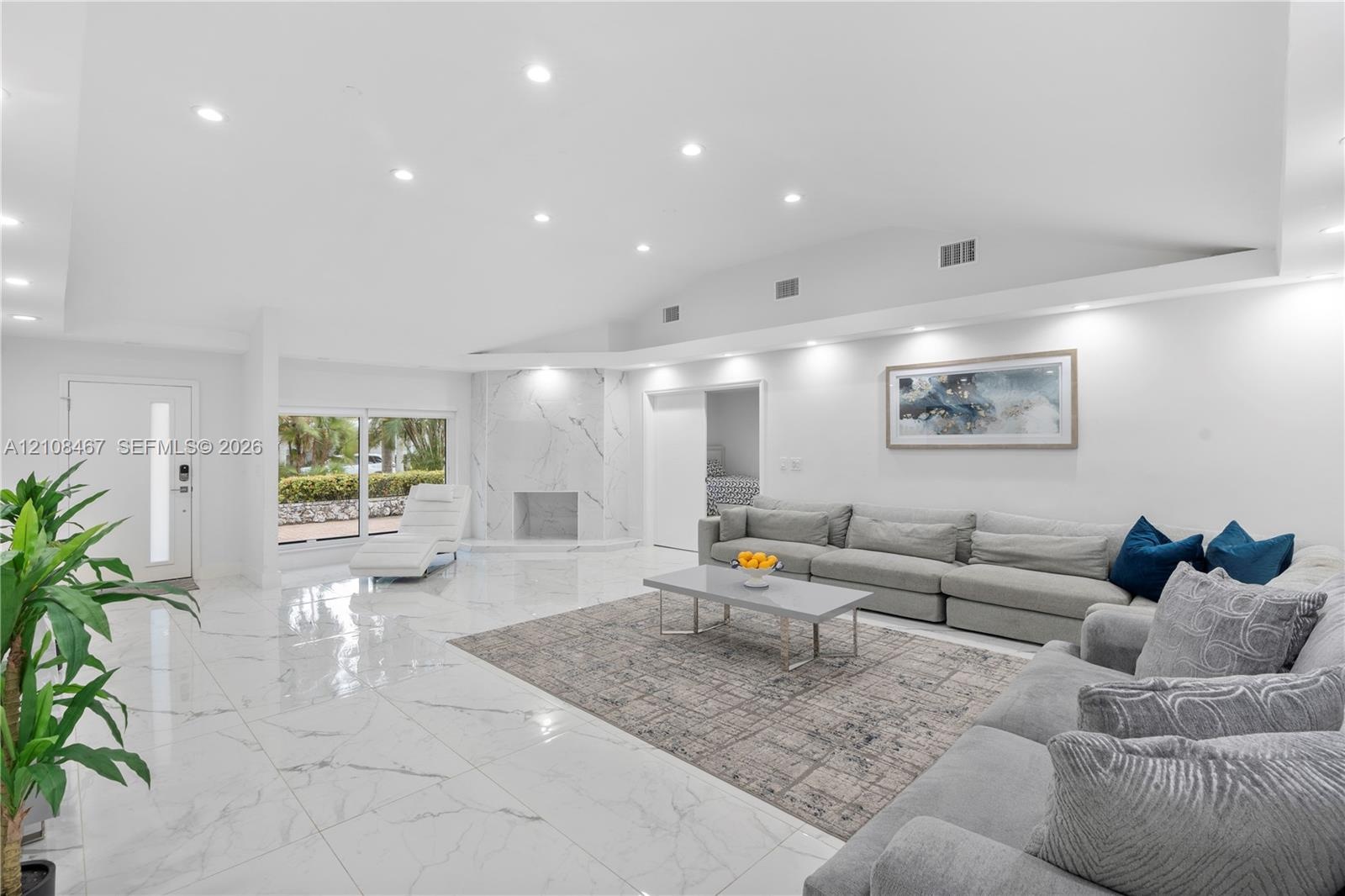 Open-concept living space featuring vaulted ceilings, polished stone-finish flooring, recessed lighting, and a floor-to-ceiling stone-surround firepla