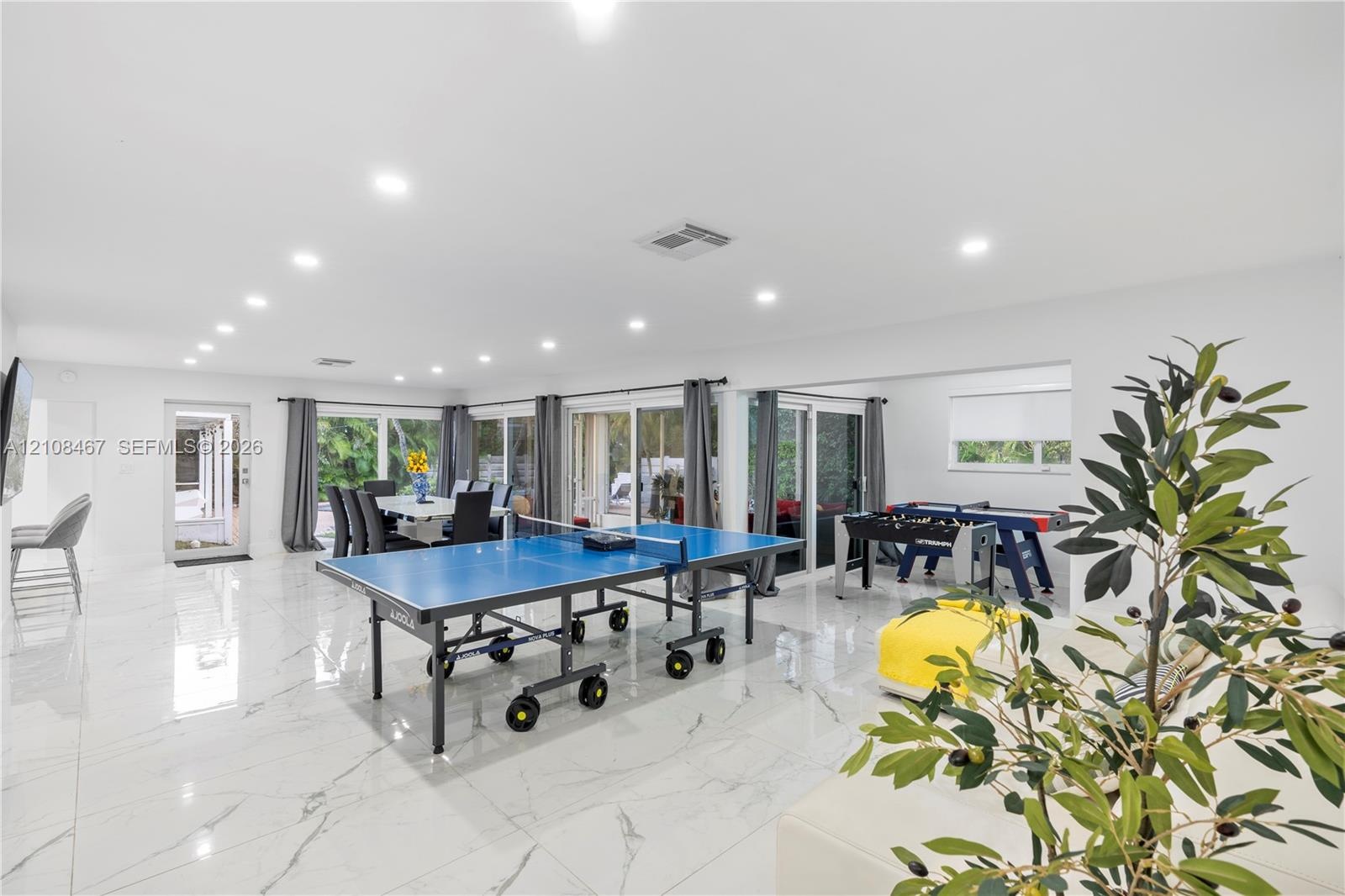 Open-concept interior featuring large-format tile flooring, recessed ceiling lighting, and multiple sliding glass doors providing access to the exteri