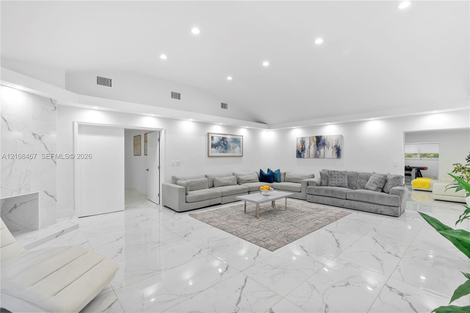 Open-concept interior featuring high vaulted ceilings, large-format tile flooring with a neutral finish, and a floor-to-ceiling stone-surround firepla
