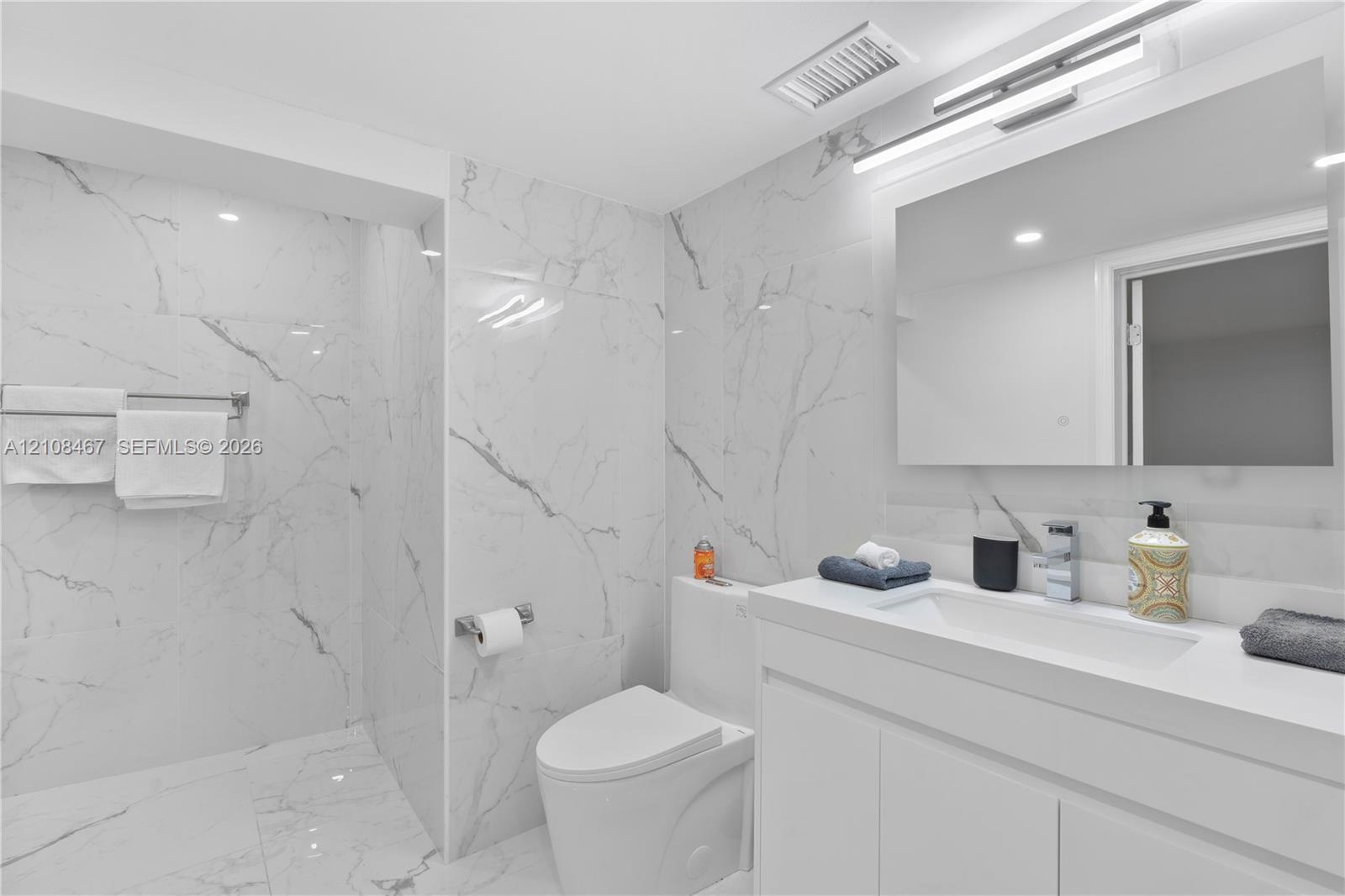 Bathroom featuring floor-to-ceiling large-format tile with marble-pattern finish, vanity with integrated sink and countertop, frameless wall-mounted m
